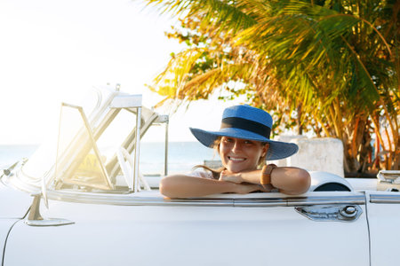 Beautiful woman in blue hat and white retro cabriolet on the beach