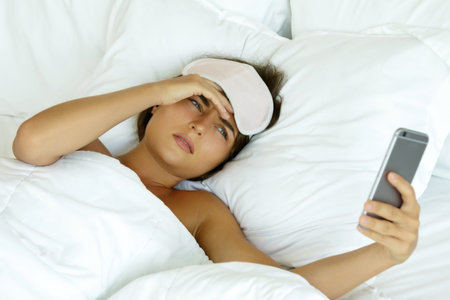 Sleepy woman looking on smartphone and don't want to wake up