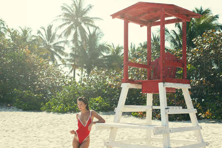 Sexy woman  in red swimsuit posing beside a lifeguard tower on the beachの写真素材