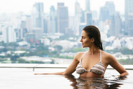 Woman relaxing on a rooftop pool with a beautiful city view on backgroundの写真素材