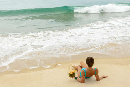 Happy woman with a coconut on the beachの写真素材