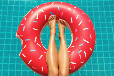 Female legs and inflatable swim ring in shape of donut in the poolの写真素材