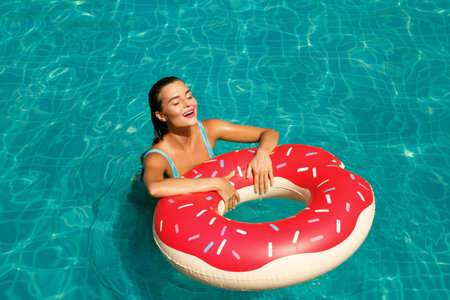 Beautiful woman and inflatable swim ring in shape of a donut in the pool