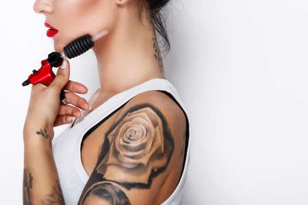Young woman tattooist with a tattoo-machine in her hand on white backgroundの写真素材