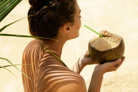 Woman with coconut drink under palm leaf on the beachの写真素材
