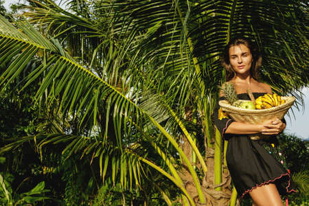 Happy young woman with a basket full of exotic fruits in the tropical gardenの写真素材