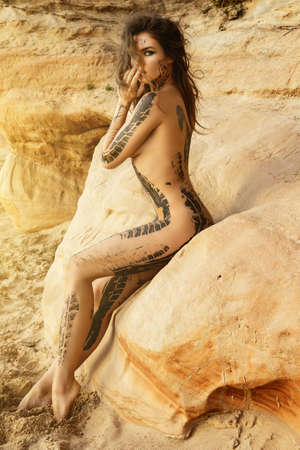 Beautiful naked woman with trace of car tire on her body is posing beside the sand cliffsの写真素材