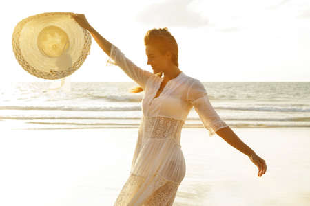 Portrait of beautiful young woman with broad-brimmed hat on the beach at sunsetの写真素材