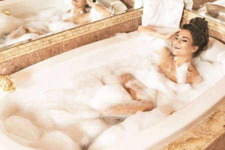 Happy and beautiful woman is taking bath with a foam in luxury apartmentsの写真素材