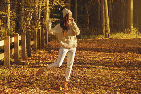 Young woman wearing warm sweater and woolen hat in the park at sunny autumn day