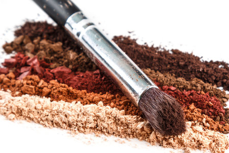 Crushed eyeshadows and make-up brushes on white background