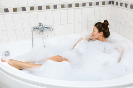 Young and beautiful woman is taking bath with a foamの写真素材