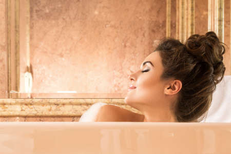 Happy and beautiful woman is taking bath with a foam in luxury apartmentsの写真素材