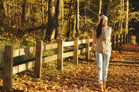 Young woman wearing warm sweater and woolen hat in the park at sunny autumn dayの写真素材