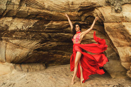 Beautiful sensual woman wearing luxury red dress and posing beside the sand cliffsの写真素材