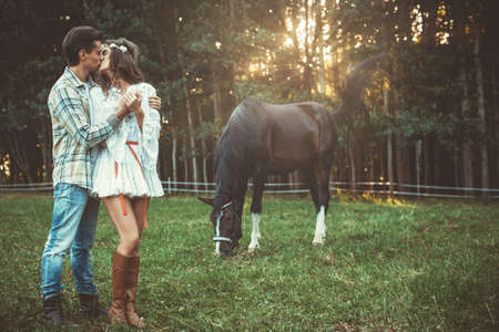 Young and happy couple in embrace on the meadow with a horsesの写真素材