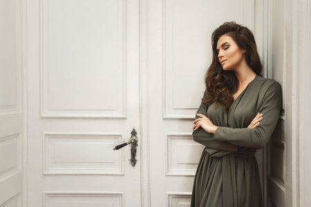 Young and gorgeous woman in beautiful dress is posing beside a big old doors