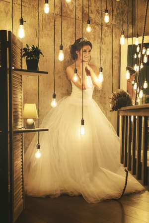 Young happy bride wearing beautiful lush dress in the room with a lot of light bulbsの写真素材