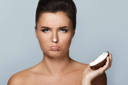 Disappointed woman with a coconut cream over gray backgroundの写真素材
