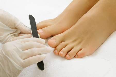 Pedicure master during work. Closeup of female feet and hands in gloves with a nail file.の写真素材