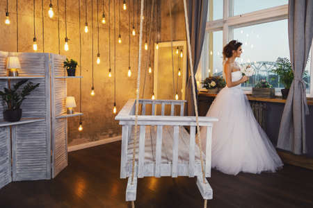 Young happy bride wearing beautiful lush dress in the room with a lot of light bulbsの写真素材
