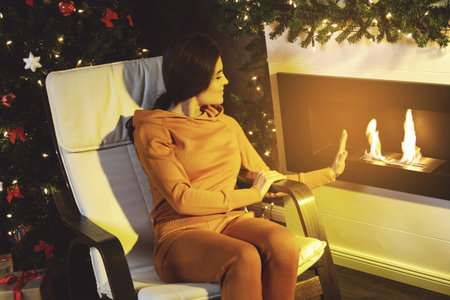 Christmas or New Year celebration. Happy woman sitting in the rocking chair beside fireplace.