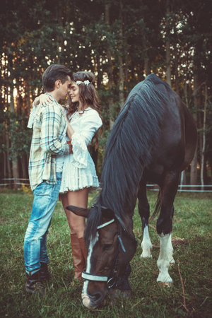 Young and happy couple in embrace on the meadow with a horsesの写真素材
