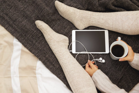 Woman in warm woolen stockings is drinking hot coffee at cold winter day