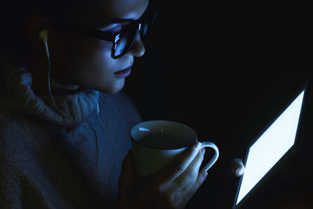Young woman wearing a warm pullover is using tablet PC in the middle of the nightの写真素材
