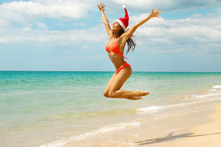 Sexy woman wearing bikini and Christmas hat on the beach. Winter holidays in the warm countries.の写真素材