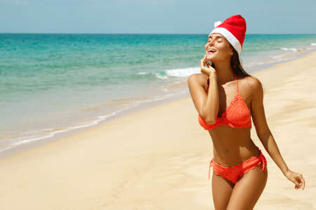 Sexy woman wearing bikini and Christmas hat on the beach. Winter holidays in the warm countries.の写真素材