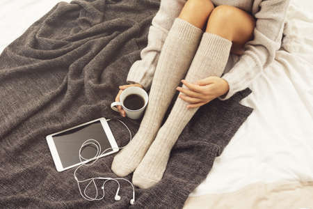 Woman in warm woolen stockings is drinking hot coffee at cold winter dayの写真素材