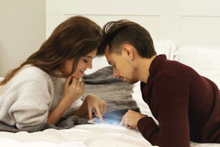 Young couple in warm sweaters is playing game on the tablet pcの写真素材