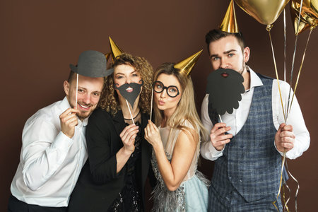 Group of happy people wearing party hats with funny photo booth props are celebrating holiday or...