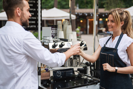 Beautiful woman barista selling coffee to the customer