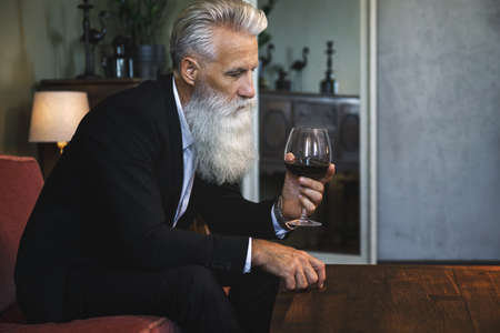 Handsome bearded senior man drinking red wineの写真素材