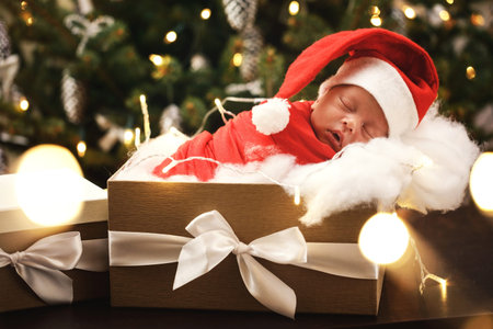 Cute newborn baby wearing Santa Claus hat is sleeping in the Christmas gift boxの写真素材