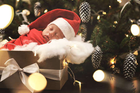 Cute newborn baby wearing Santa Claus hat is sleeping in the Christmas gift boxの写真素材