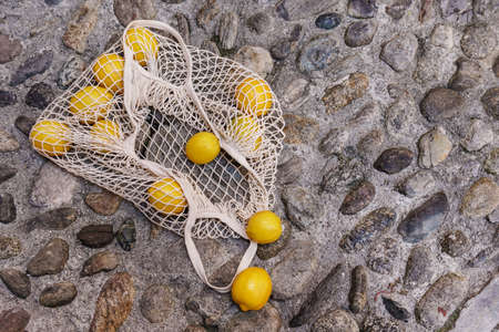 Net bag with a heap of fresh lemons lying on the cobblestoneの写真素材