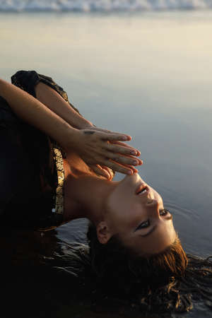 Sexy woman wearing black tunic is posing on the beach with black sandの写真素材