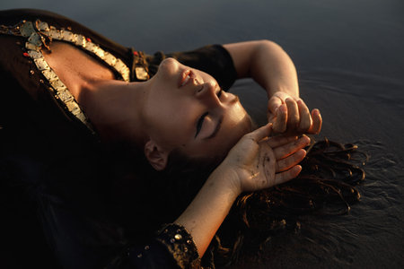Sexy woman wearing black tunic is posing on the beach with black sand