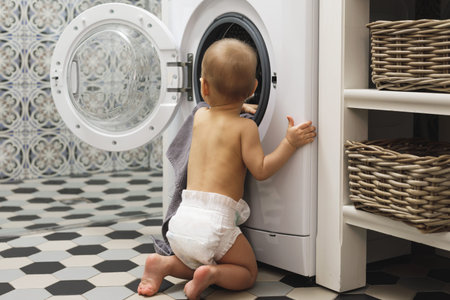 Cute baby boy is looking inside the washing machine