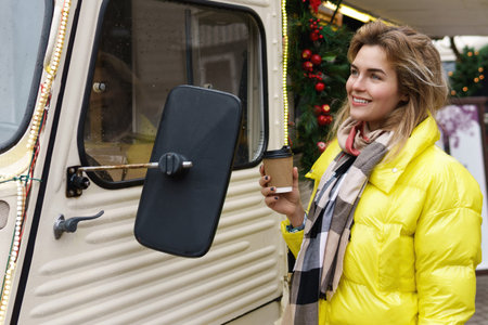 Happy woman with a cup of hot coffee beside the retro van at Christmas market