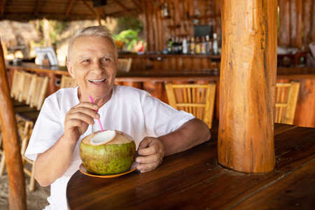Happy senior man is drinking a coconut water in the beach barの写真素材