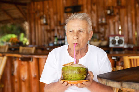 Happy senior man is drinking a coconut water in the beach barの写真素材