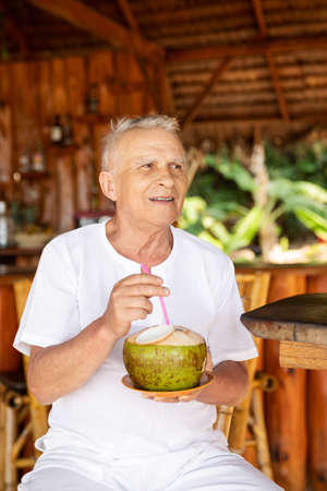 Happy senior man is drinking a coconut water in the beach barの写真素材