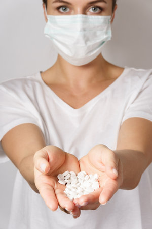 Woman wearing face mask is holding a white pillsの写真素材