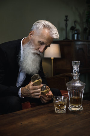 Handsome and bearded senior man drinking whiskey