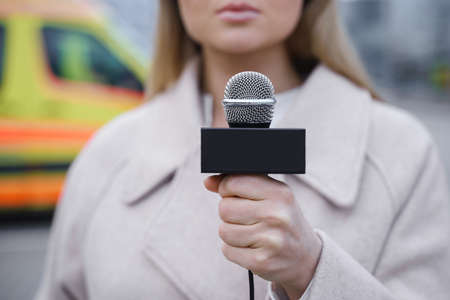 Journalist speaking into the microphone beside the ambulance vehicleの写真素材