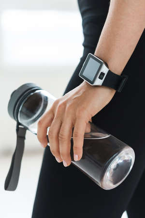 emale hand with smartwatch holding reusable bottle with water.の写真素材